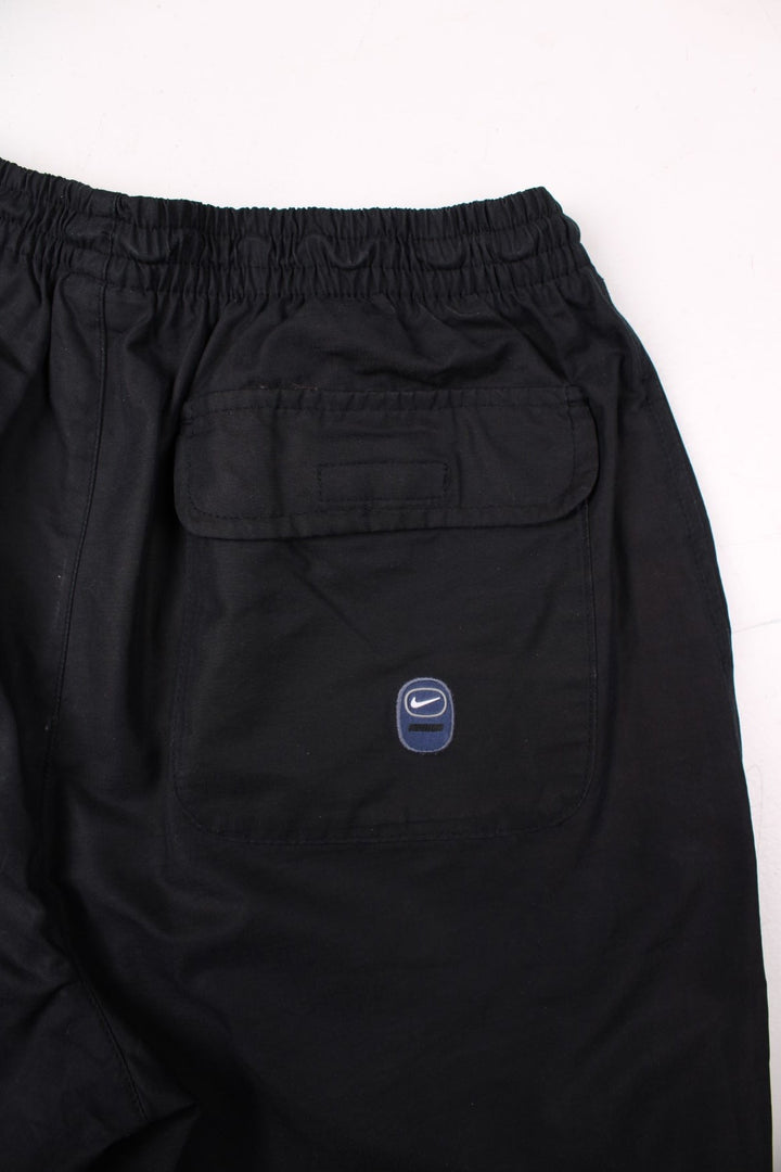 Nike Swoosh shorts in black with an elasticated waist, fake button detail, multiple pockets and several Nike Swoosh logo patches.