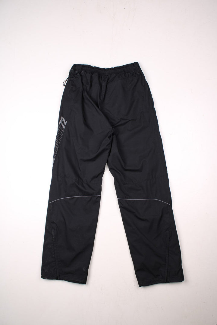 Nike Athletic 72 tracksuit bottoms in black with an elasticated waist, a toggle adjuster, two pockets, a printed spellout up the left leg, and an embroidered logo on the front.