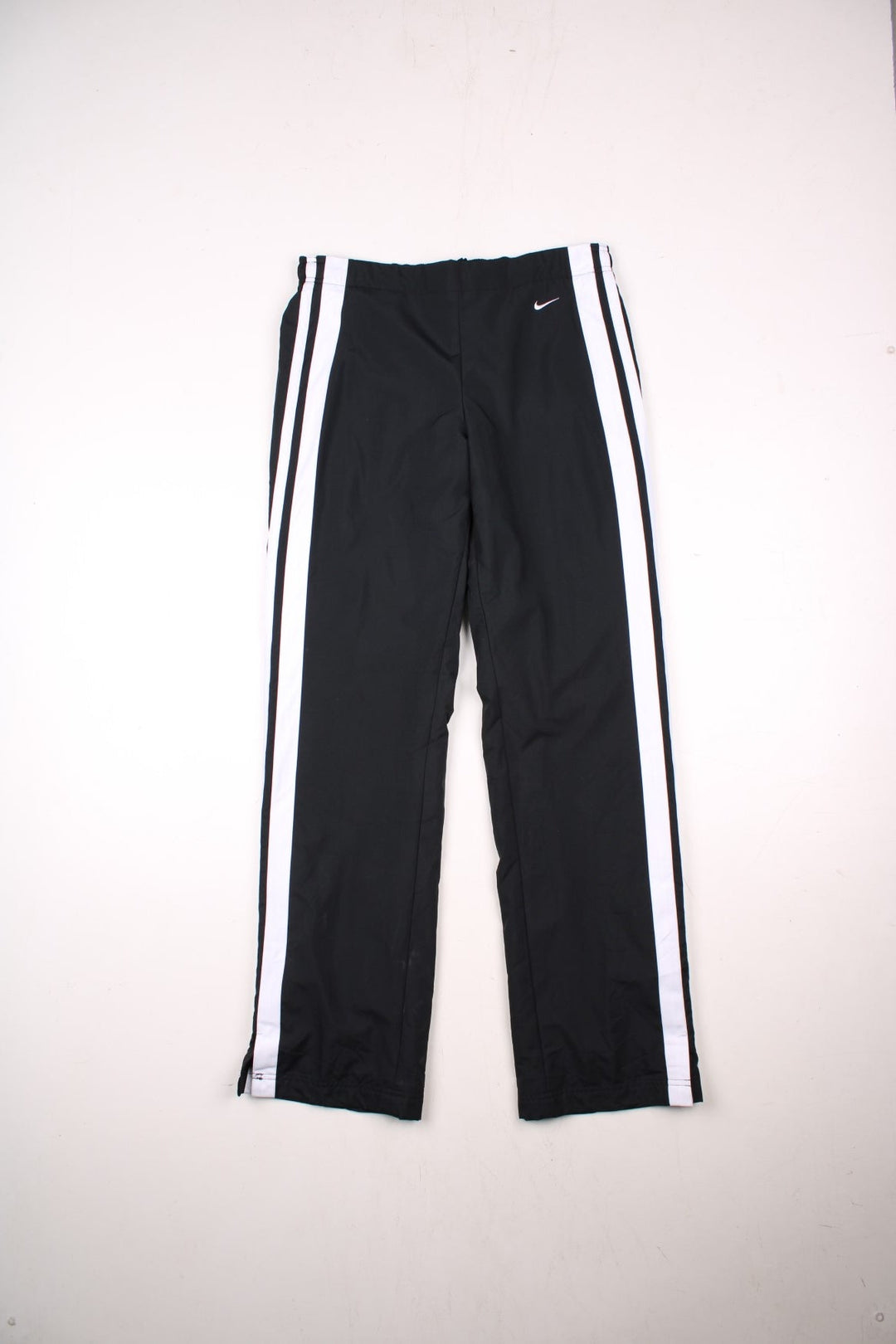 Nike tracksuit bottoms in black with white stripe detailing, two pockets, an elasticated waist, and an embroidered logo on the front.