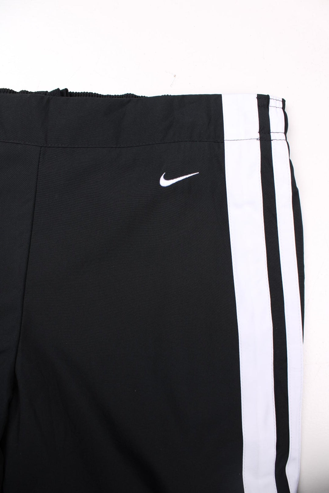 Nike tracksuit bottoms in black with white stripe detailing, two pockets, an elasticated waist, and an embroidered logo on the front.