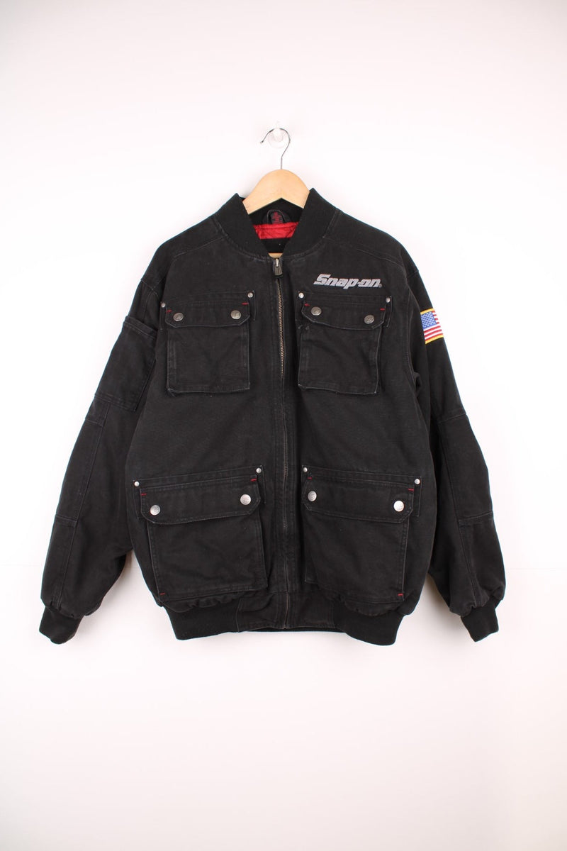 Vintage Snap On Tools zip through canvas bomber jacket with multiple pockets. Features embroidered logo on the chest, USA flag badge on the sleeve, and embossed silver buttons and studs.