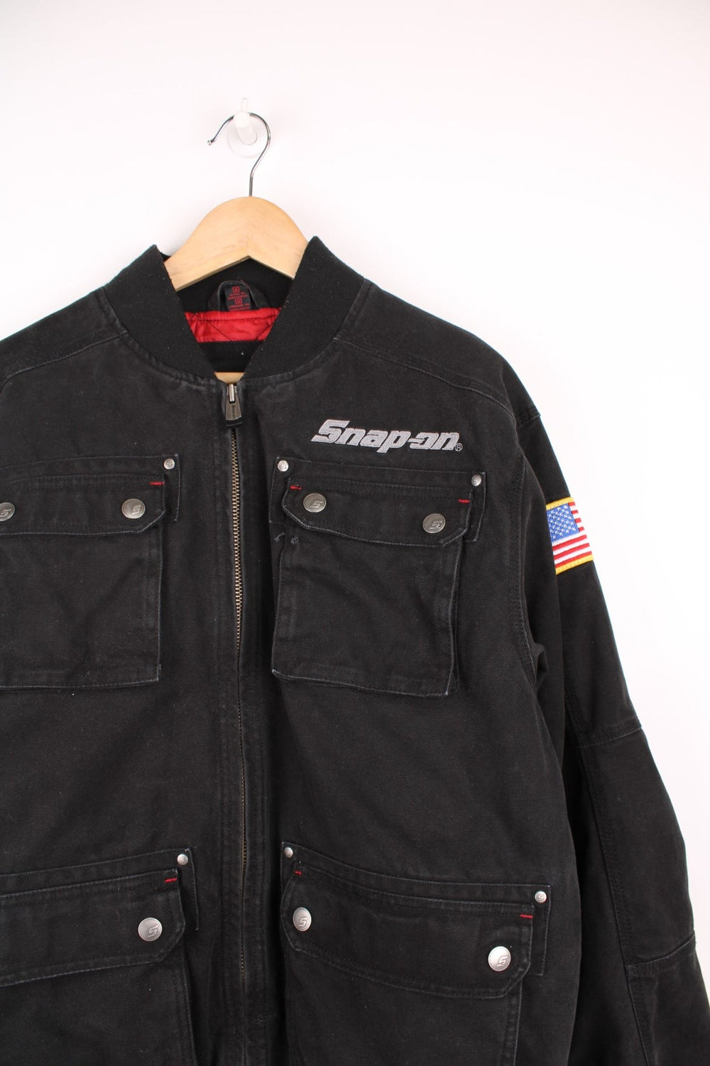 Vintage Snap On Tools zip through canvas bomber jacket with multiple pockets. Features embroidered logo on the chest, USA flag badge on the sleeve, and embossed silver buttons and studs.