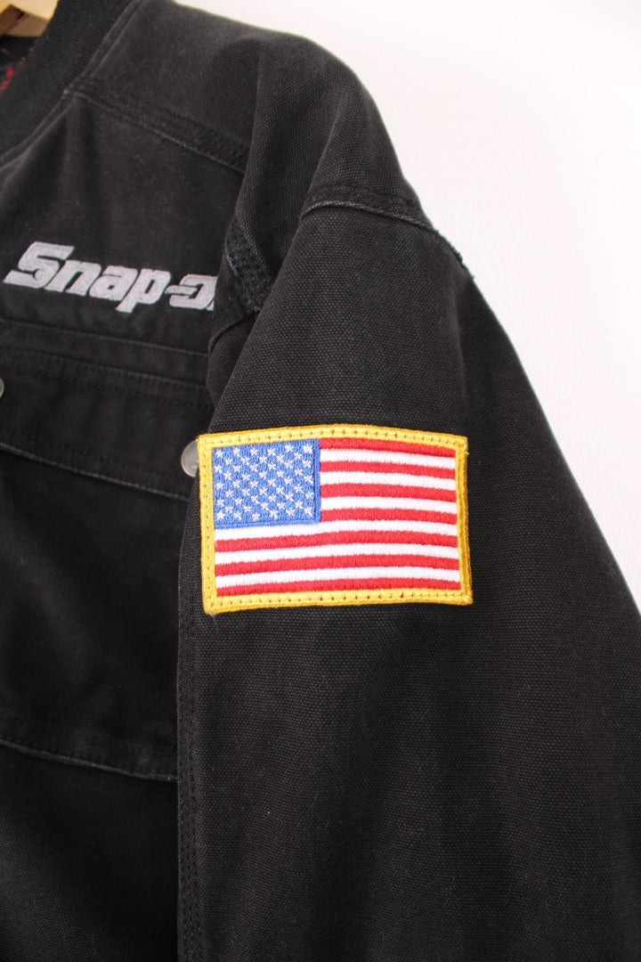 Vintage Snap On Tools zip through canvas bomber jacket with multiple pockets. Features embroidered logo on the chest, USA flag badge on the sleeve, and embossed silver buttons and studs.