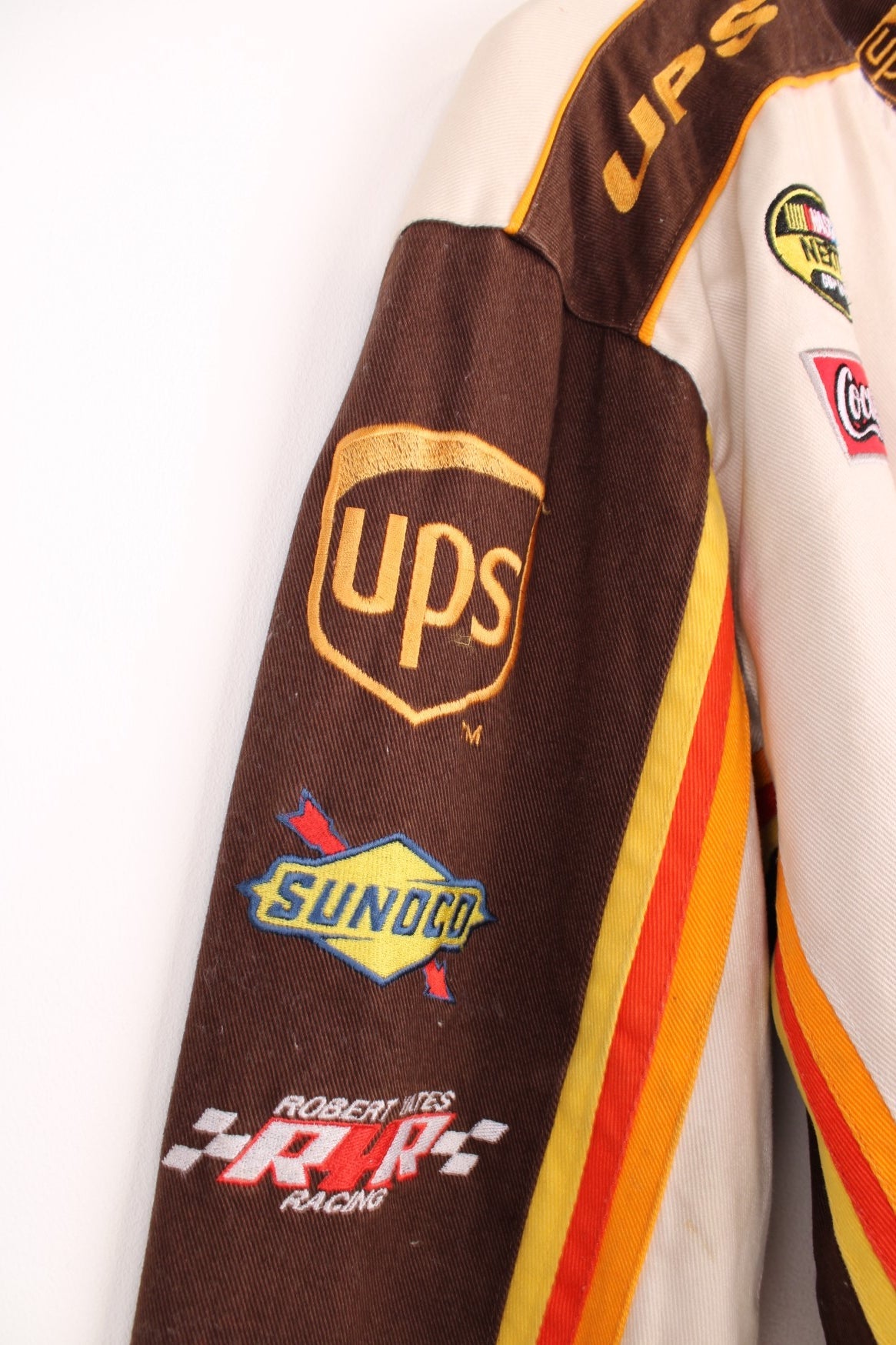 Vintage Dale Jarrett UPS NASCAR jacket by Chase Authentics in brown and orange. Features embroidered sponsor badges all over.  