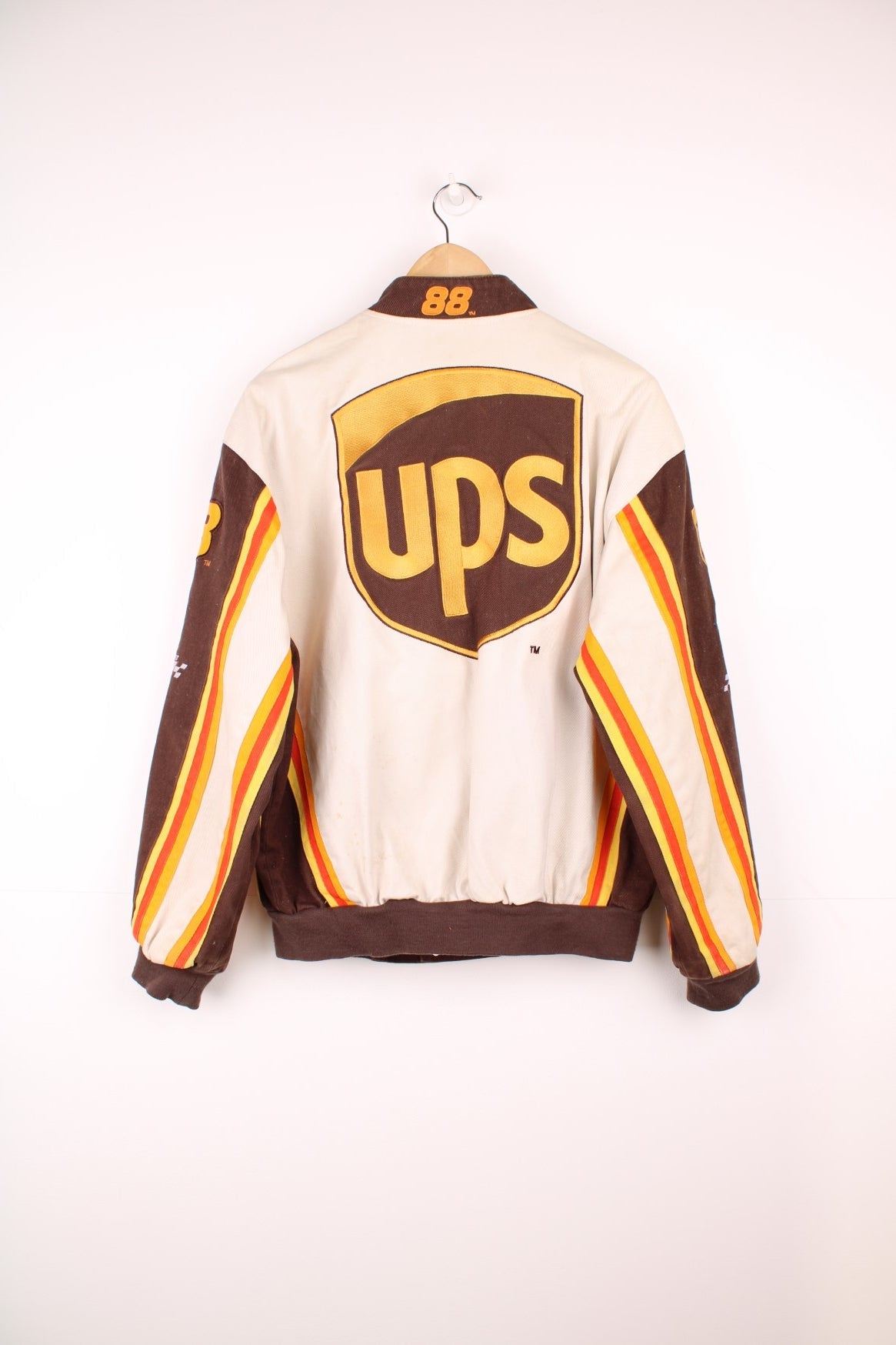 Vintage Dale Jarrett UPS NASCAR jacket by Chase Authentics in brown and orange. Features embroidered sponsor badges all over.  