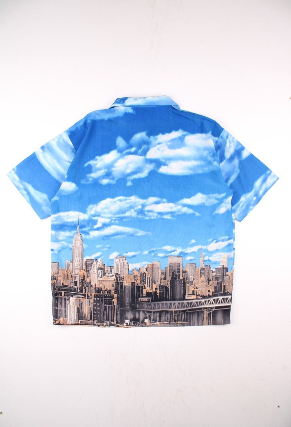 Vintage Northpeak shirt in blue with print of the New York City skyline against a blue sky and clouds.