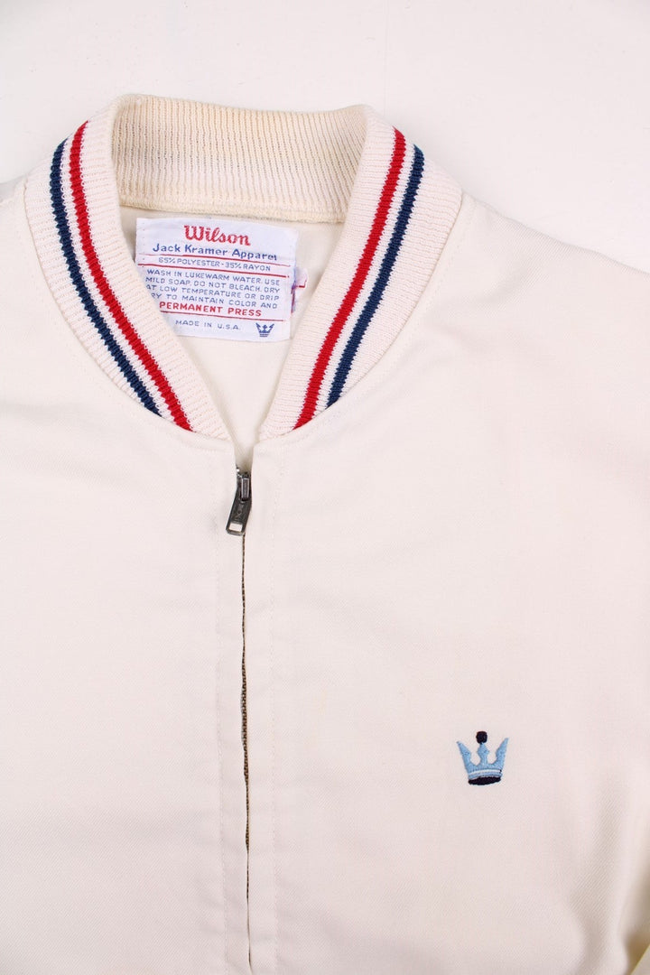 Vintage 1950's Wilson Athletics Jack Kramer made in the USA tennis jacket in white with zip closure, two pockets, red and blue srtipe detailing on the collar and cuffs, and an embroidered crown logo on the chest.