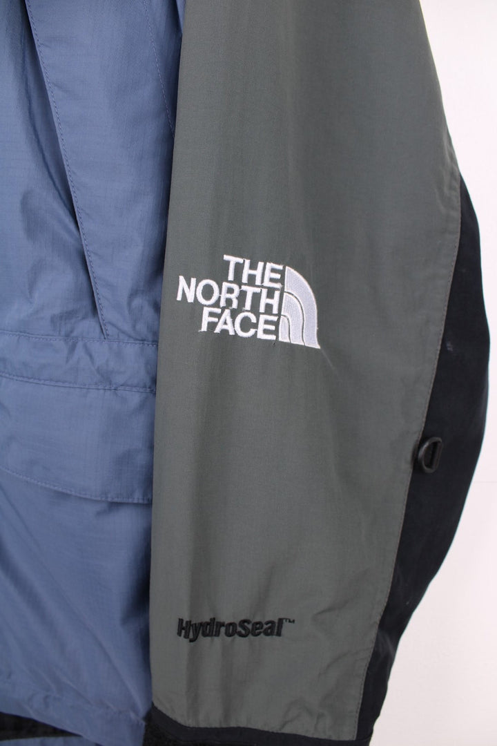 The North Face Hydroseal blue and grey zip through waterproof jacket. Features multiple pockets, foldaway hood and embroidered logo on the sleeve