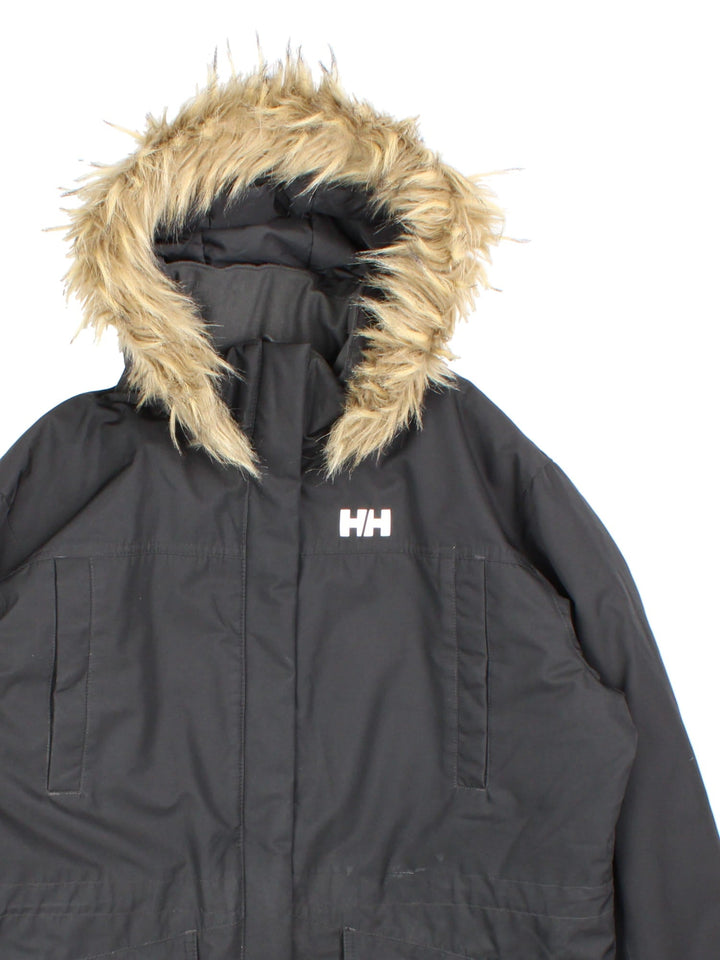 Helly Hansen Parka Coat in a black colourway. Multiple pockets on front and has a faux fur parka hood and the logo on the front.