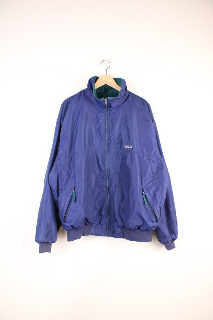 Patagonia Synchilla Jacket in a blue colourway with a green fleece lining, zip up with side pockets, and has the logo embroidered on the front. 