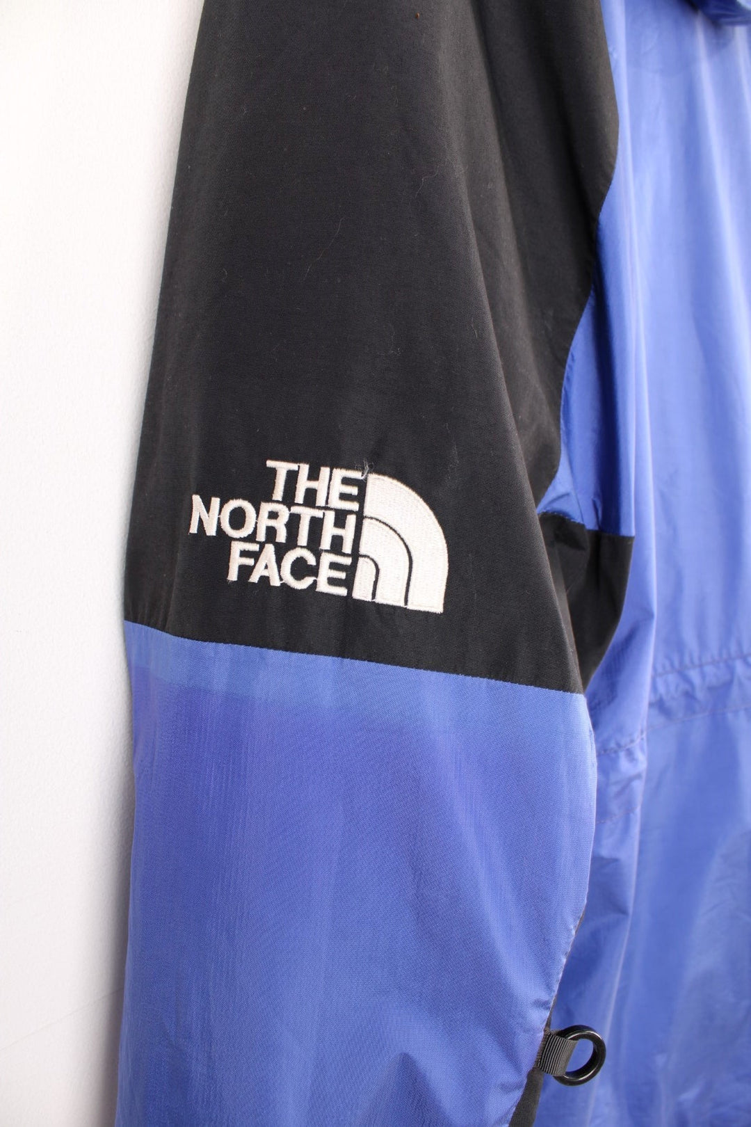 The North Face Mountain Light Gore-Tex Jacket in a blue and black colourway, zip up with side pockets, hooded, has a mesh lining, and the logo embroidered on the left sleeve. 