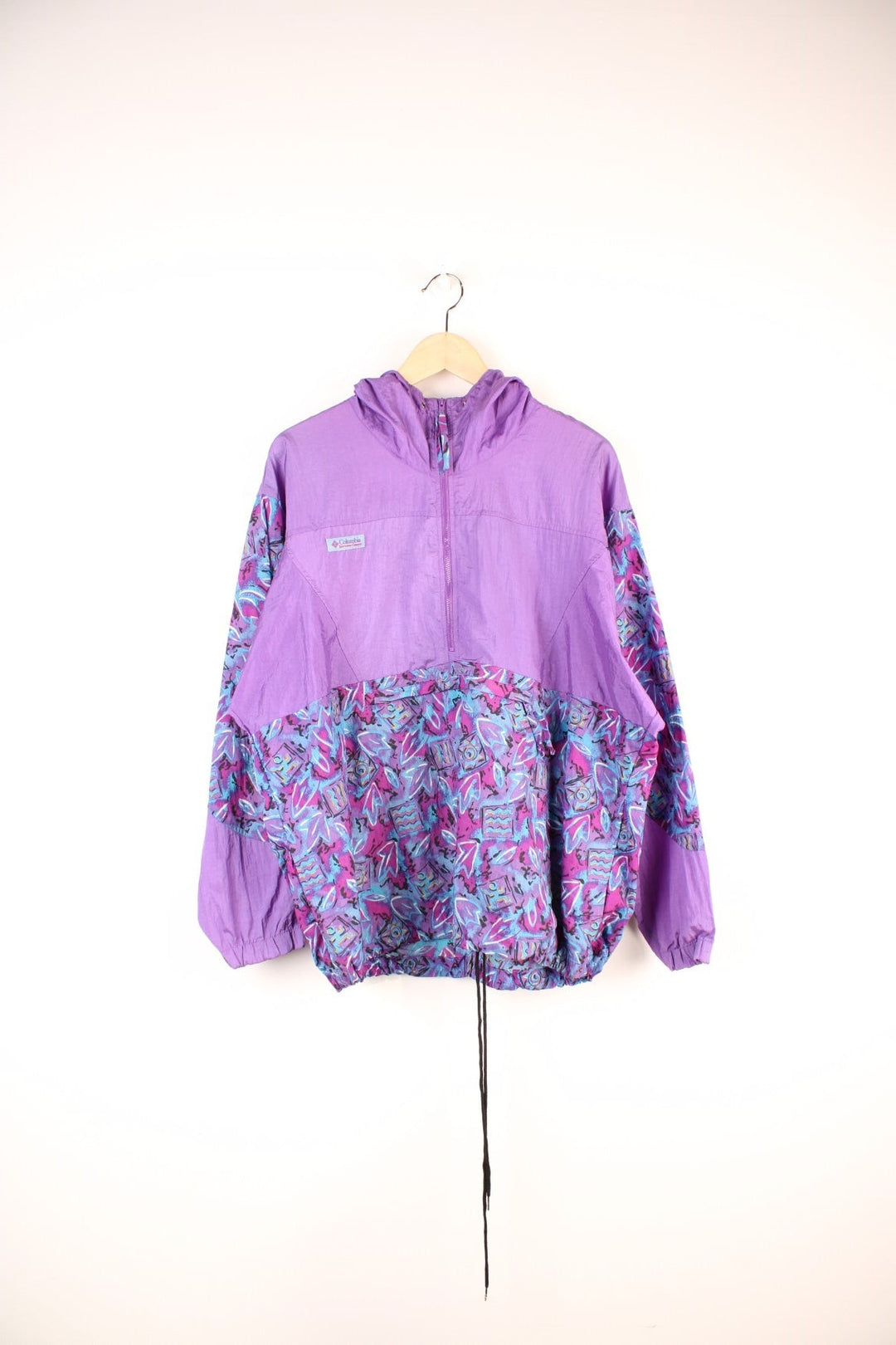 90's Columbia Patterned Windbreaker in a purple and blue colourway, surf style sportswear, half zip with pouch pockets, has adjustable waist line toggles, hooded and has the logo embroidered on the front. 