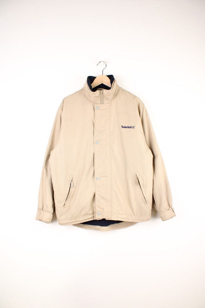 Timberland Jacket in a tanned colourway, zip and button up, side pockets, has a hideable hood, insulated with a fleece lining, and has the logo embroidered on the front and back. 