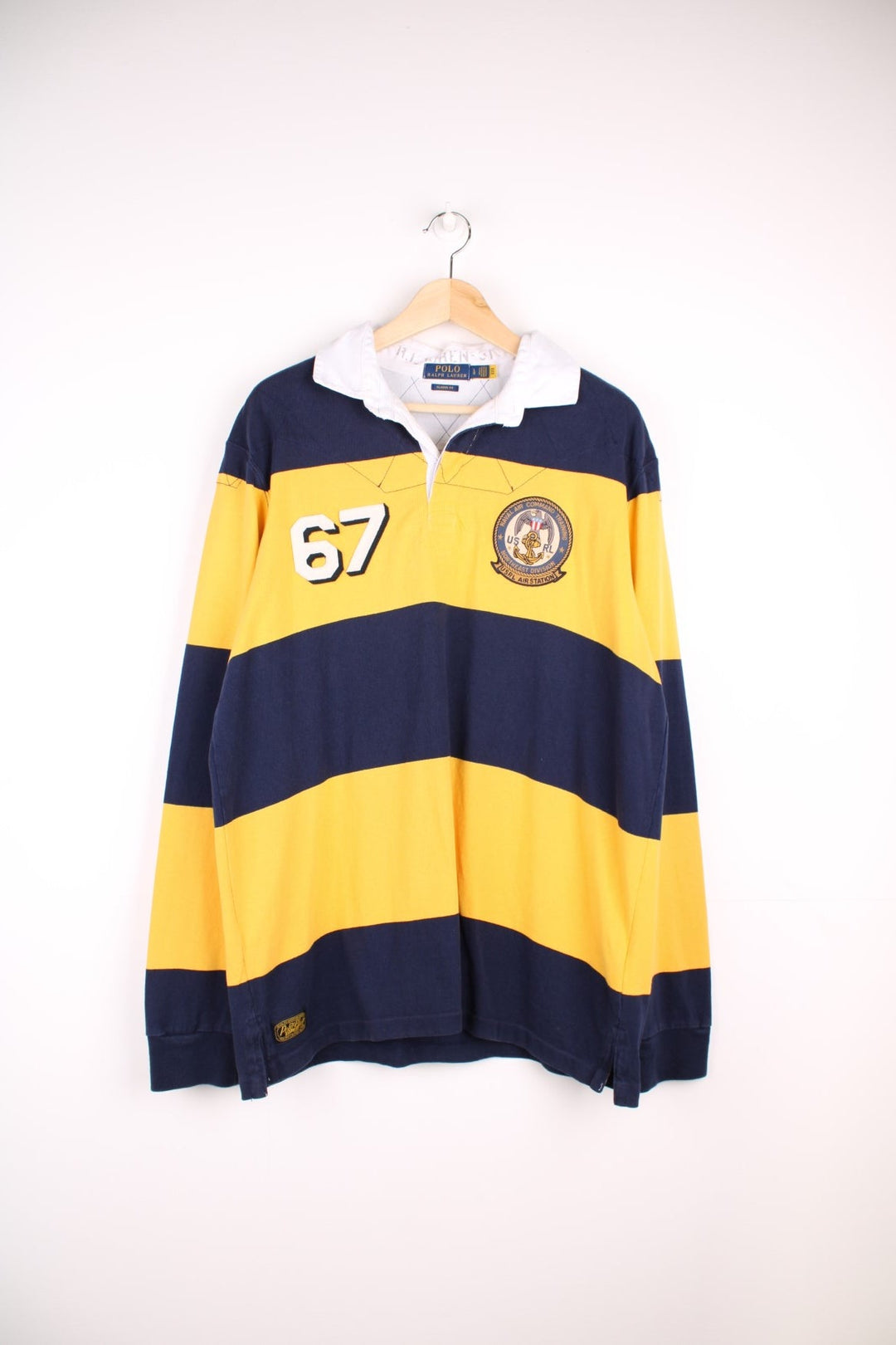 Ralph Lauren striped rugby shirt in yellow and navy stripe with the Ralph Lauren logo and graphics printed on the front. There is also a large team logo patch on the back.