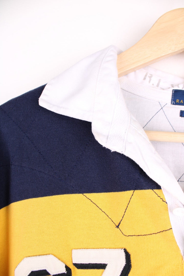 Ralph Lauren striped rugby shirt in yellow and navy stripe with the Ralph Lauren logo and graphics printed on the front. There is also a large team logo patch on the back.