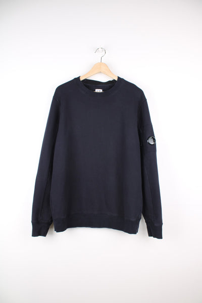C.P. Company Sweatshirt in a navy blue colourway, has the goggle lens on the left sleeve on the pocket, and also has the spell out logo printed on the back of the neck lining.