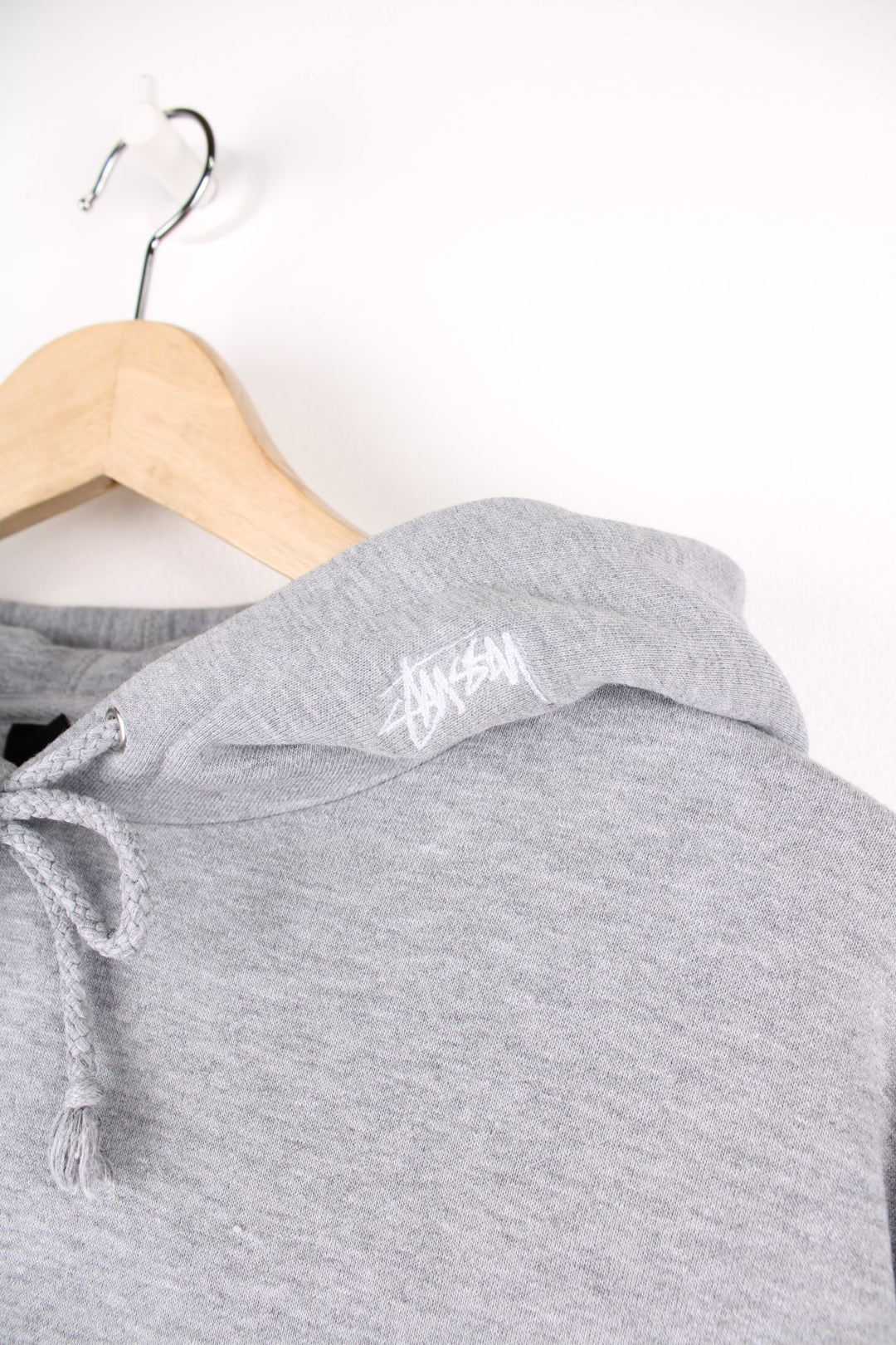 Stussy Logo Hoodie in a grey colourway with the spell out logo embroidered across the front in a brown and white colourway, also has 'XXV' embroidered onto the hood alongside the logo, and has a pouch pocket.