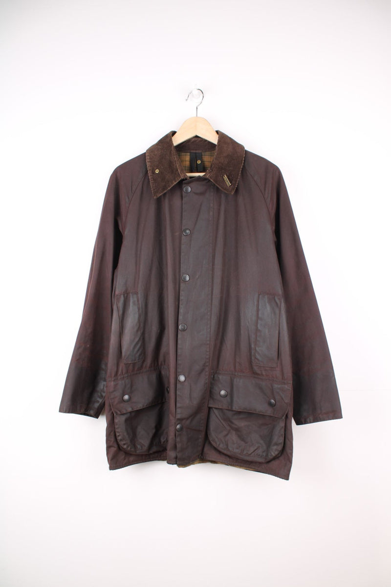 Vintage Barbour Beaufort Wax Jacket in a burgundy brown colourway with a corduroy collar that has a pin on it, zip up with multiple pockets, and has a tartan lining.