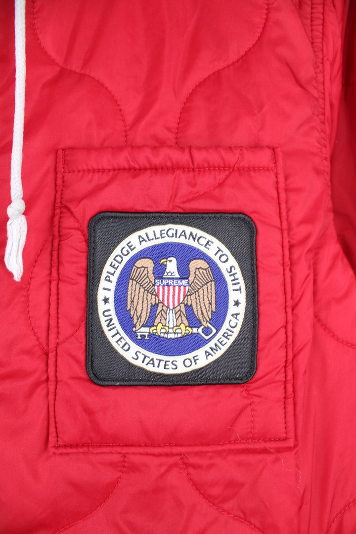 Supreme Quilted Liner Hooded Jacket in a red colourway with a grey cotton hood, "I pledge allegiance to shit, USA" badge embroidered on the front, and has multiple pockets.