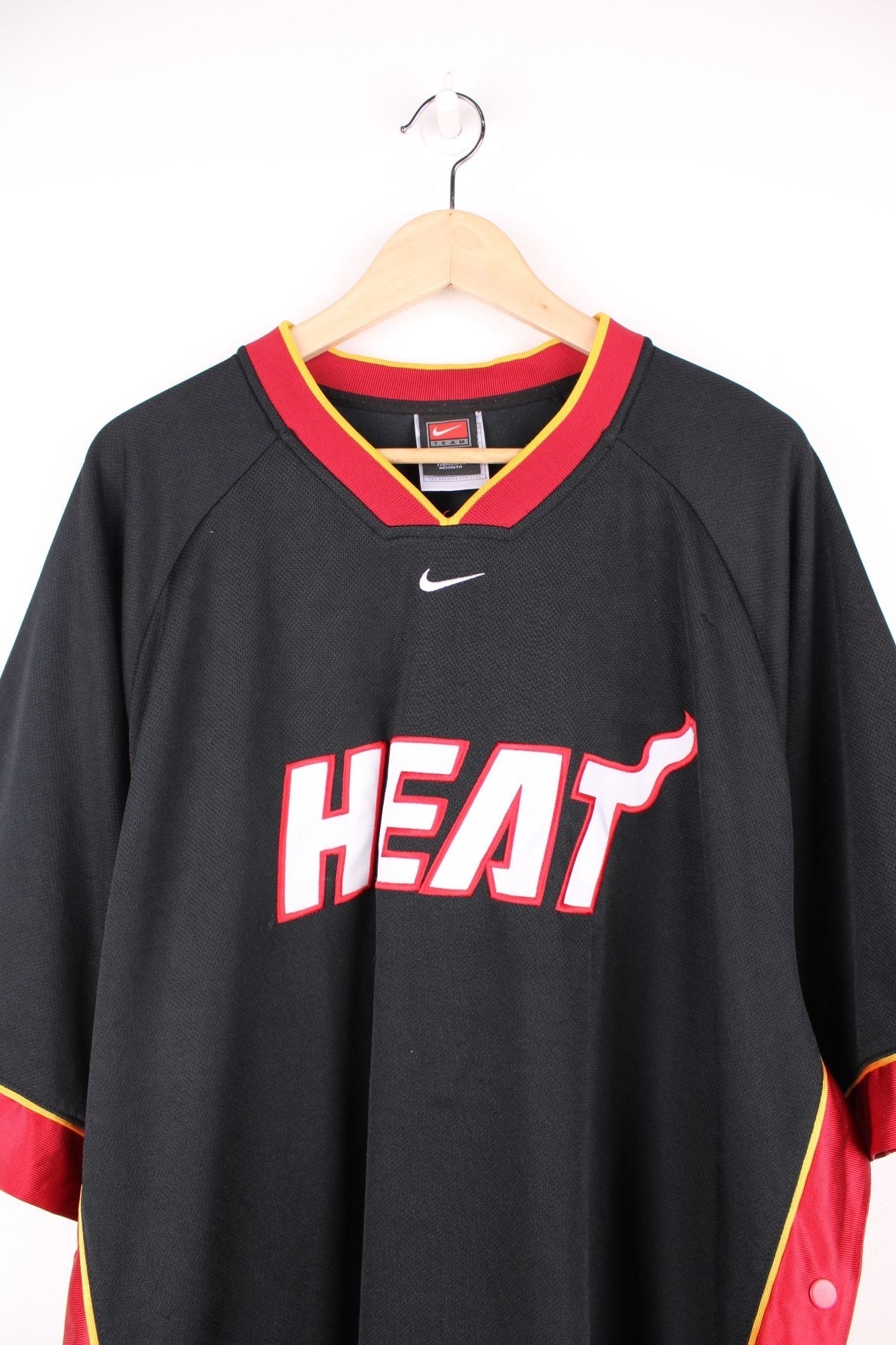 NBA Miami Heat Nike Training Jersey in a black and red colourway, popper buttons going down the side and under arms, v neck, and has the logos embroidered on the front. 