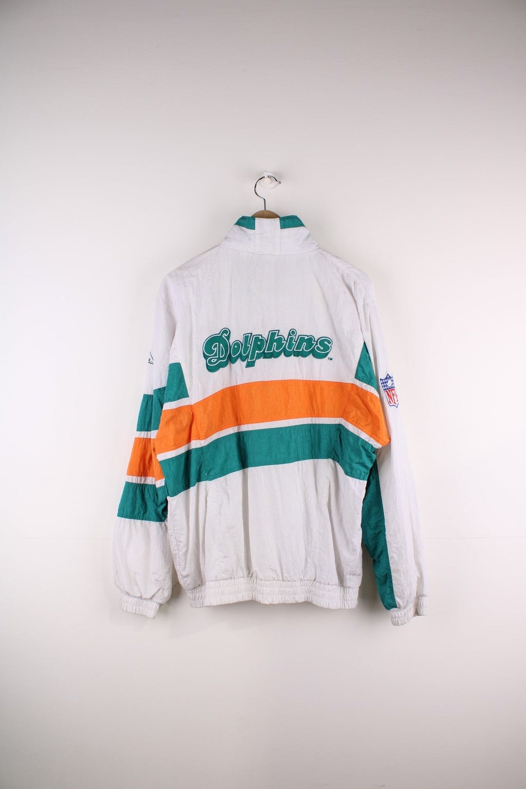 Miami Dolphins NFL Jacket in white with turquoise and orange stripes, the dolphin logo on the chest and script on the back, and Apex and NFL logos on each sleeve.