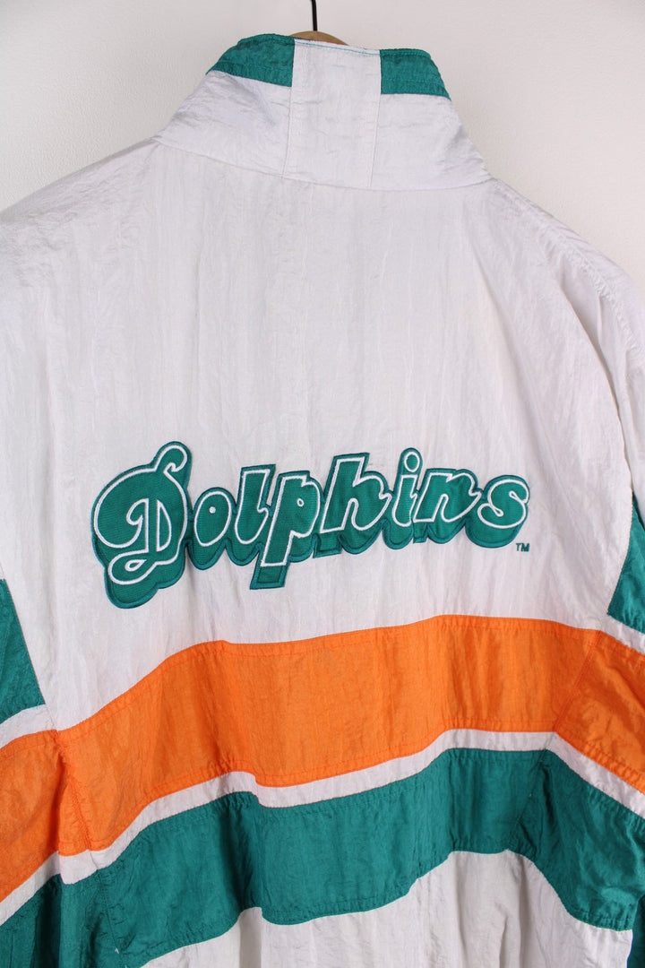 Miami Dolphins NFL Jacket in white with turquoise and orange stripes, the dolphin logo on the chest and script on the back, and Apex and NFL logos on each sleeve.