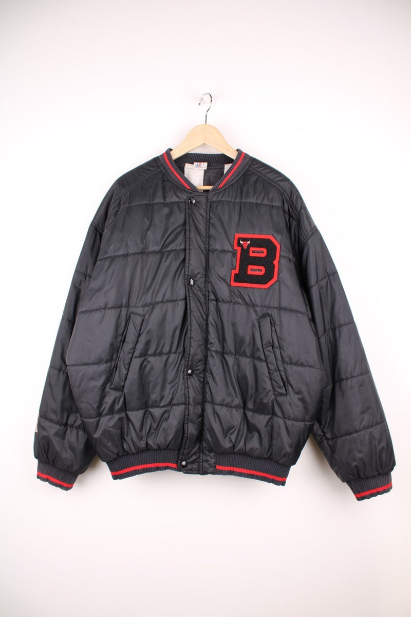 NBA Chicago Bulls Puffer Coat in a black and red colourway, zip up with side pockets, insulated lining, and has the logo embroidered on the front. 