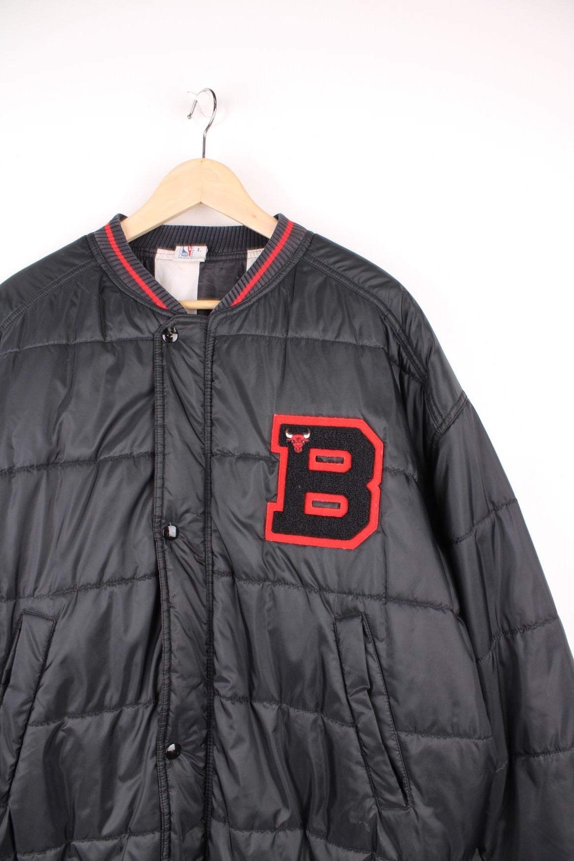 NBA Chicago Bulls Puffer Coat in a black and red colourway, zip up with side pockets, insulated lining, and has the logo embroidered on the front. 