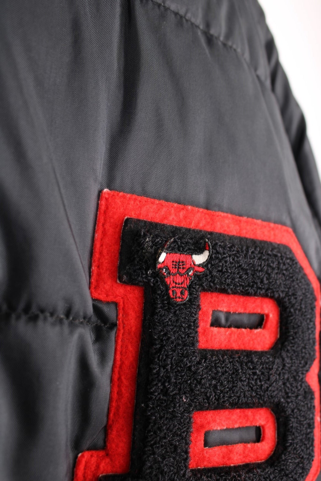 NBA Chicago Bulls Puffer Coat in a black and red colourway, zip up with side pockets, insulated lining, and has the logo embroidered on the front. 