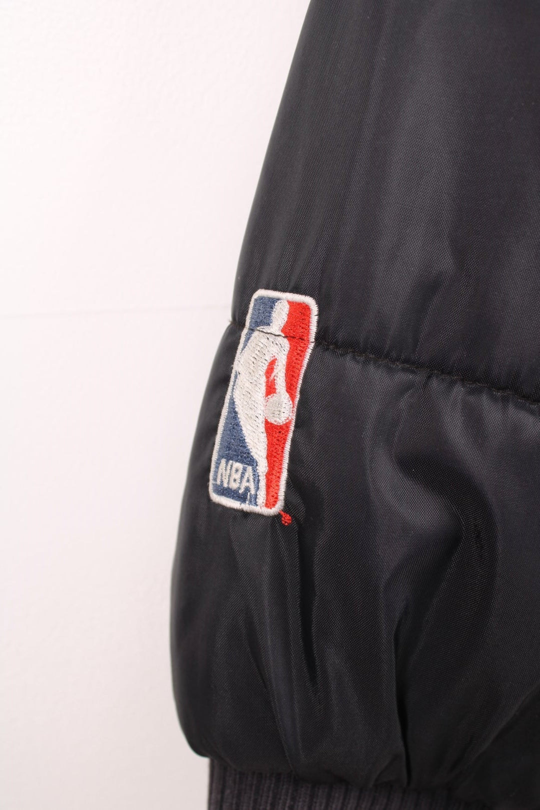 NBA Chicago Bulls Puffer Coat in a black and red colourway, zip up with side pockets, insulated lining, and has the logo embroidered on the front. 