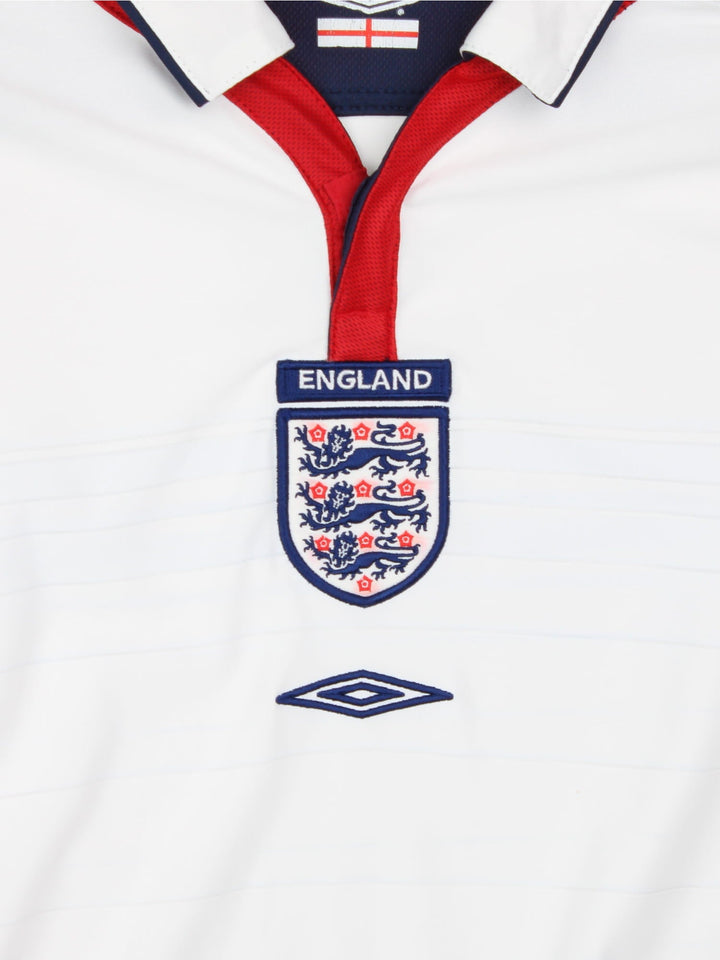 England 2003/05 Umbro home kit reversible football shirt in white with blue stripes and navy blue collar and piping on one side, red on the other. 2 snap closure at the neck, and a logo and badge on the front on both sides.