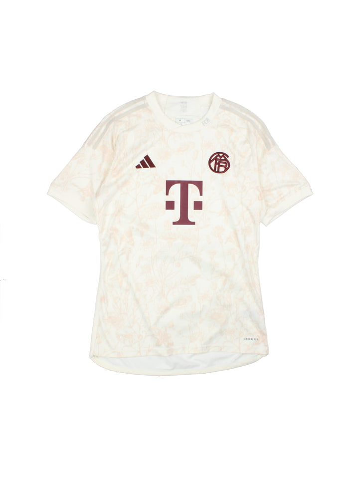 FC Bayern 2023/24 Adidas third kit football shirt in tan with subtle floral print, three stripe detailing in white, and logos and a badge on the front.