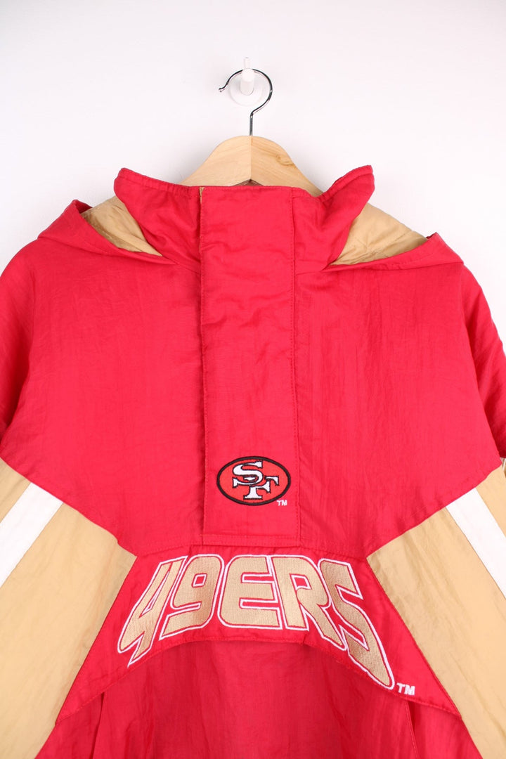 San Francisco 49ers, NFL pro sport jacket in a red colourway with beige and white side panels. Zip closure and hood, with team logos on the front, sleeve and back.