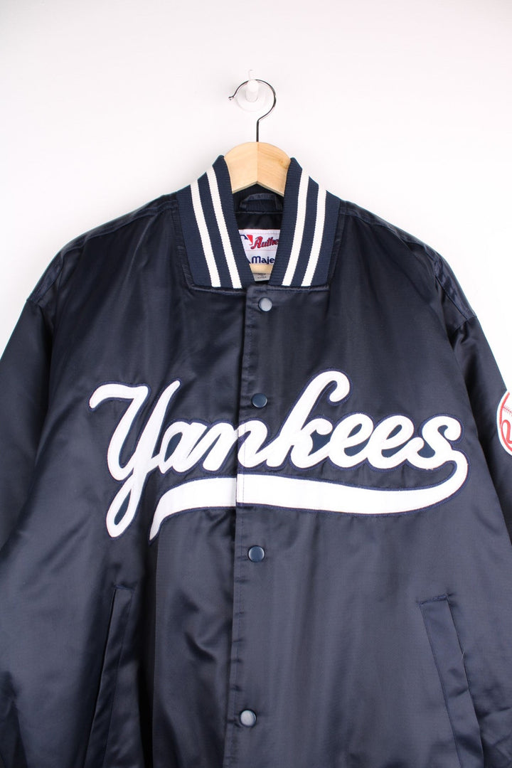 NY Yankees vintage pro sport bomber jacket in navy blue satin with white stripe detail. Snap fastener closure, with team logos embroidered on the front and sleeve.