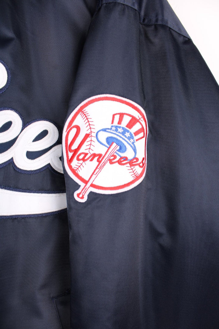 NY Yankees vintage pro sport bomber jacket in navy blue satin with white stripe detail. Snap fastener closure, with team logos embroidered on the front and sleeve.