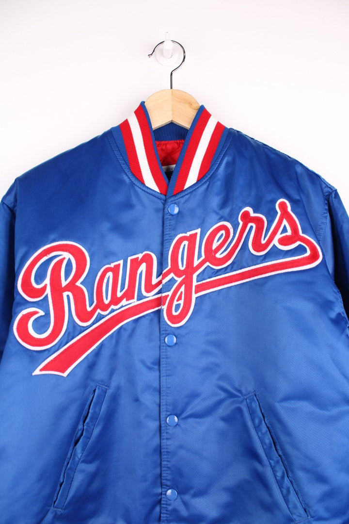 Texas Rangers pro sport jacket in a blue colourway with white and red stripe detail. Snap fastener closure with team logos embroidered on the front.