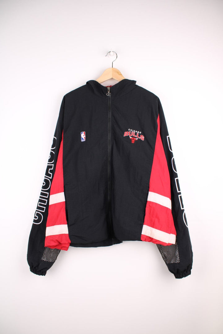 Chicago Bulls NBA pro sport jacket in a black colourway with red side panels. Full zip closure with team logos embroidered on the front and back.