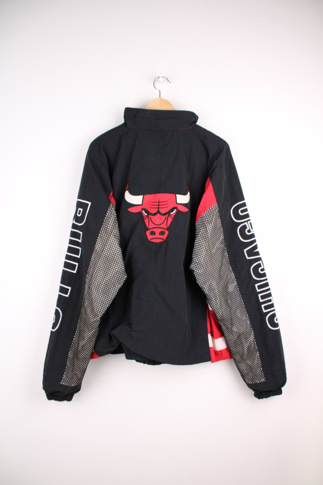 Chicago Bulls NBA pro sport jacket in a black colourway with red side panels. Full zip closure with team logos embroidered on the front and back.