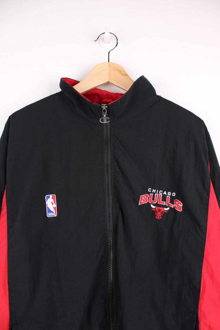 Chicago Bulls NBA pro sport jacket in a black colourway with red side panels. Full zip closure with team logos embroidered on the front and back.