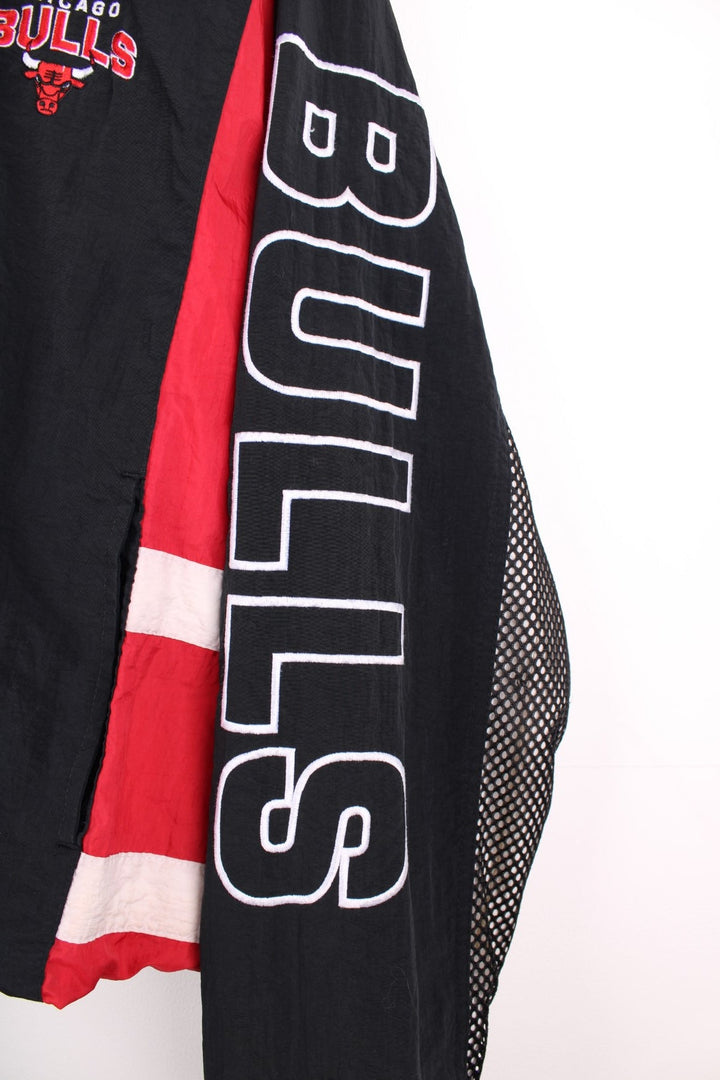 Chicago Bulls NBA pro sport jacket in a black colourway with red side panels. Full zip closure with team logos embroidered on the front and back.