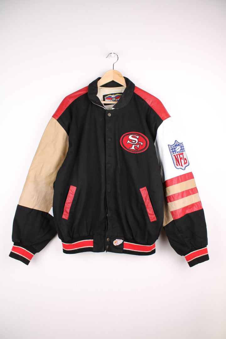 San Francisco 49s, NFL, Jeff Hamilton bomber-style pro sport jacket in a black colourway with white, red and tan detail. Zip closure with team logos embroidered on the front and back.