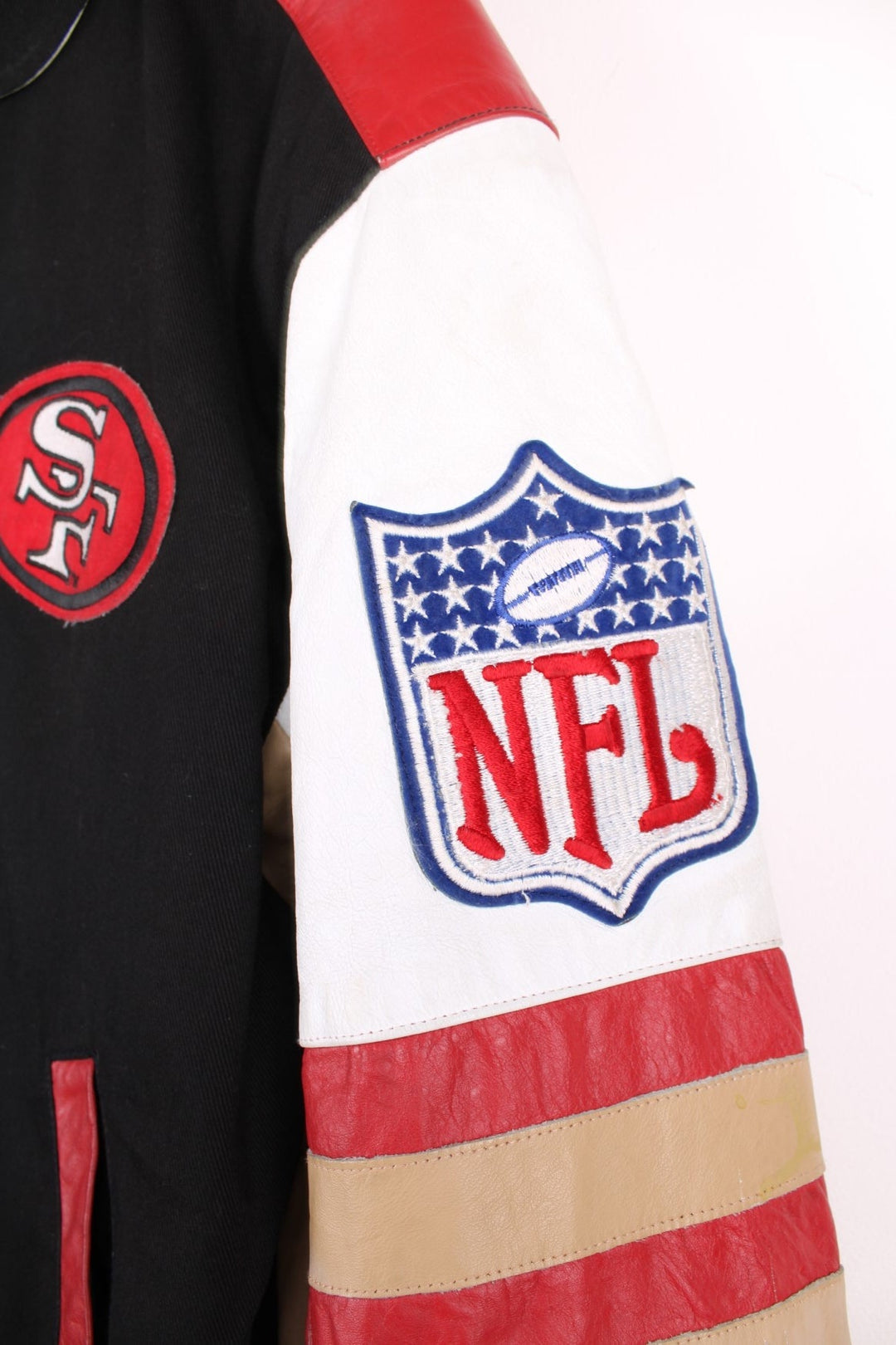 San Francisco 49s, NFL, Jeff Hamilton bomber-style pro sport jacket in a black colourway with white, red and tan detail. Zip closure with team logos embroidered on the front and back.