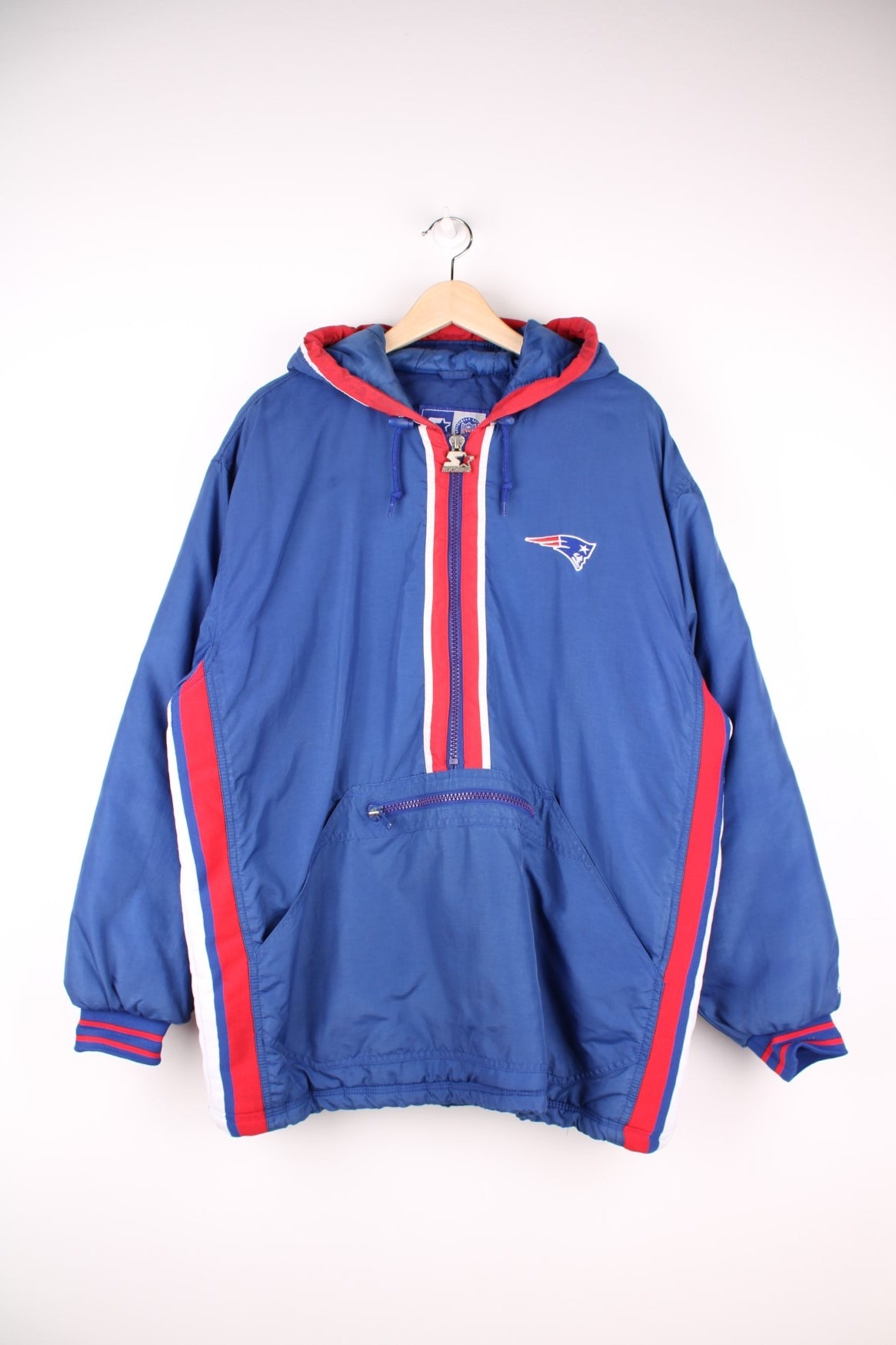 Starter NFL New England Patriots Pullover Jacket in a blue, white and red colourway, half zip up with big pouch pockets, insulated with quilted lining, hooded, and has the team logo embroidered on the front and back.