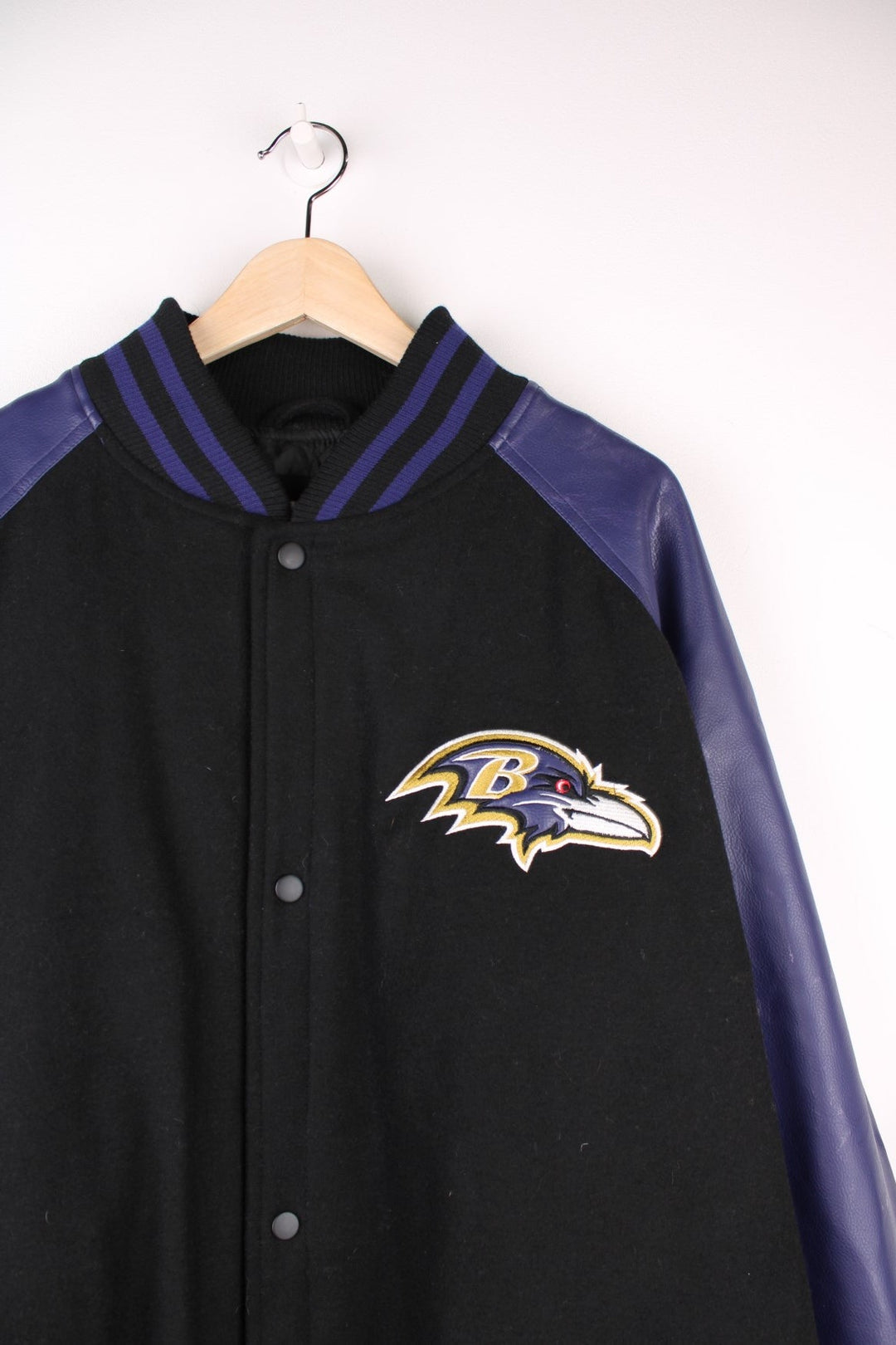 Baltimore Ravens NFL Varsity Jacket in a black and purple colourway, button up with side pockets, insulated with a quilted lining, and has the team logo and spell out embroidered on the front and back. 