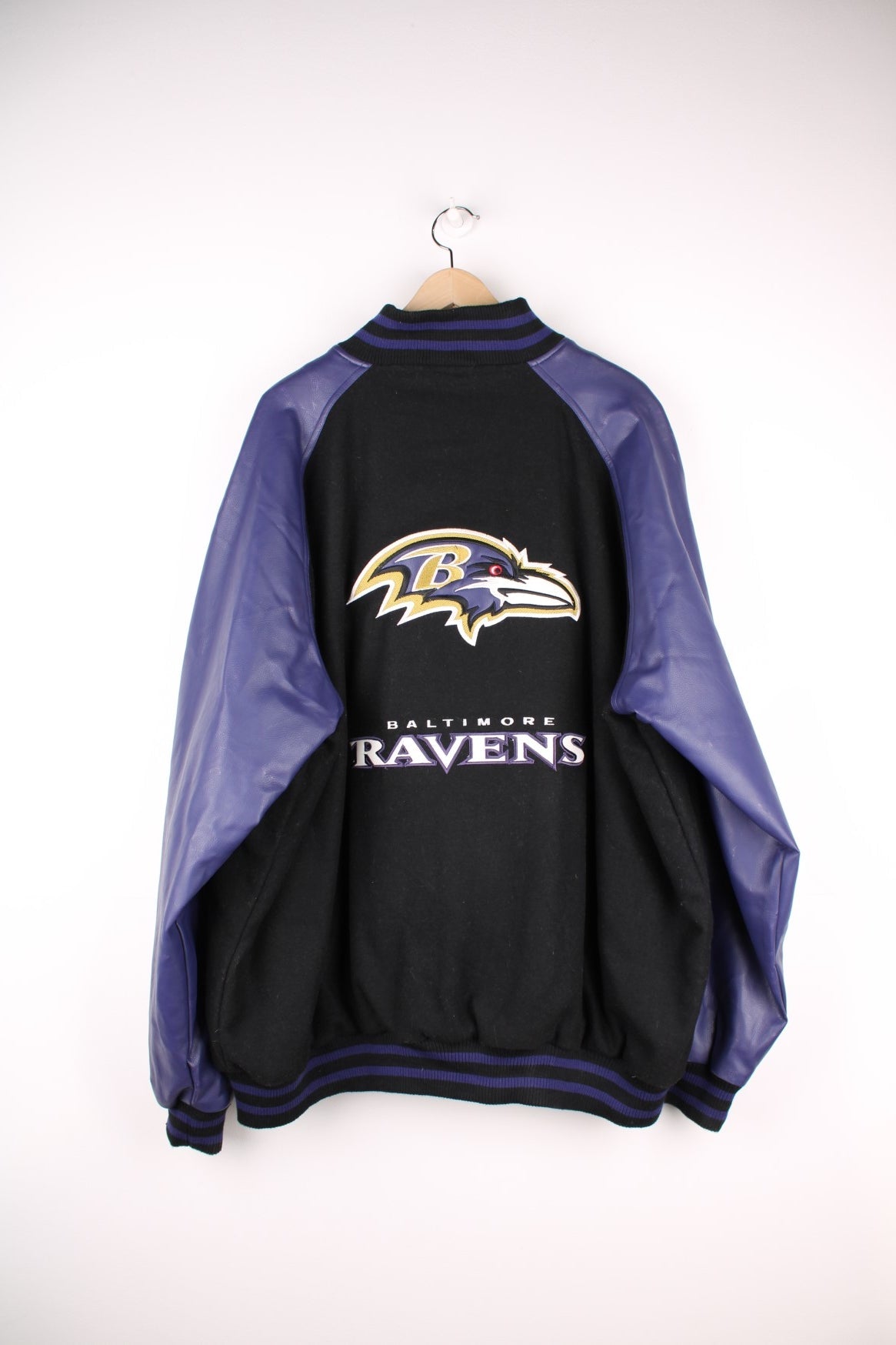 Baltimore Ravens NFL Varsity Jacket in a black and purple colourway, button up with side pockets, insulated with a quilted lining, and has the team logo and spell out embroidered on the front and back. 