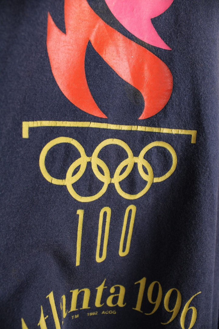 Champion 1996 Atlanta 'Centennial Olympic Games' t-shirt in navy blue with front graphic of Olympic torch, and small Champion C embroidered on the sleeve.