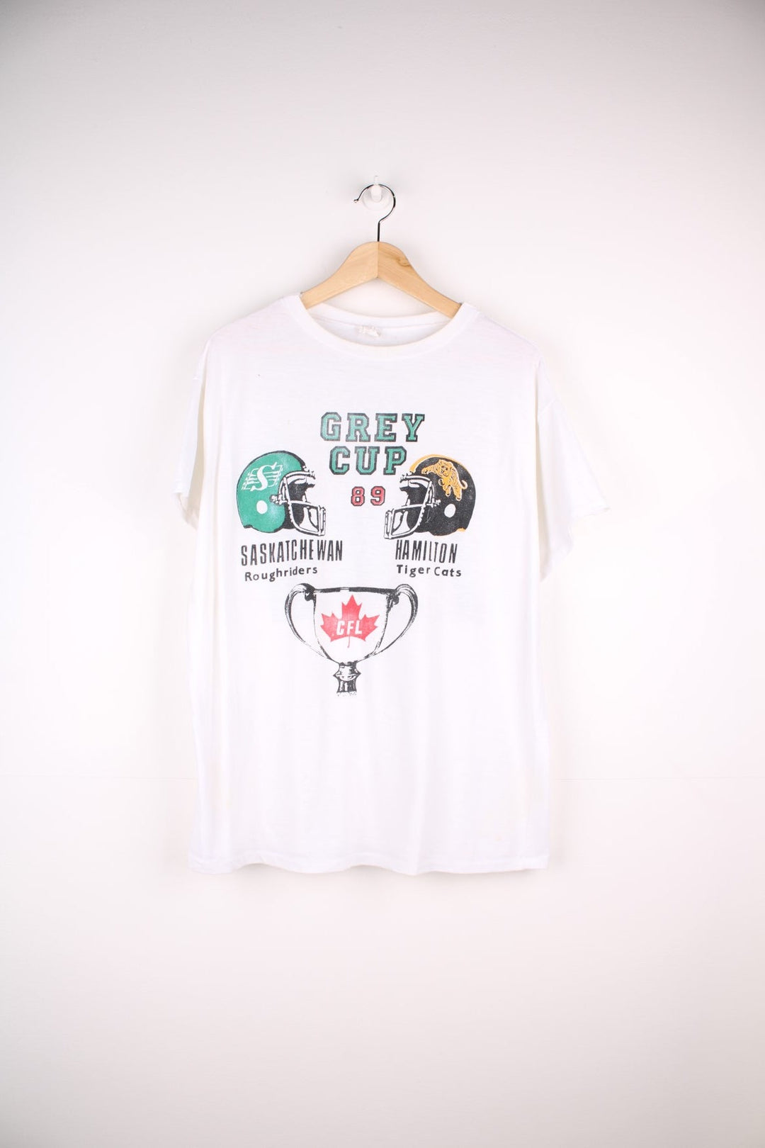 Vintage 1989 CFL Grey Cup Saskatchewan Roughriders vs Hamilton Tiger Cats tee in white with helmet face-off graphic on the front and photo of trophy on the back.