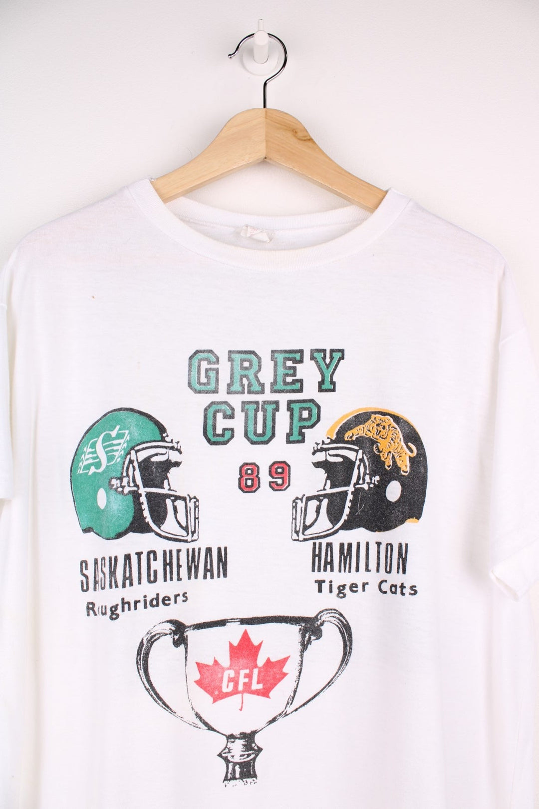 Vintage 1989 CFL Grey Cup Saskatchewan Roughriders vs Hamilton Tiger Cats tee in white with helmet face-off graphic on the front and photo of trophy on the back.