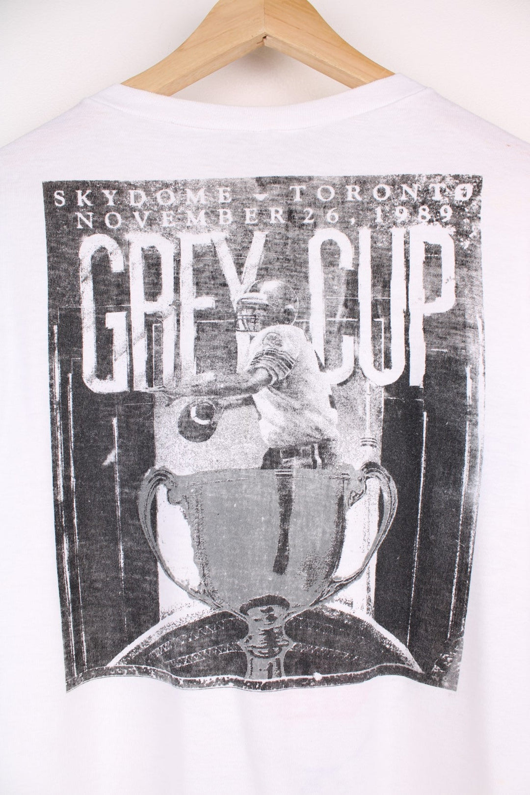 Vintage 1989 CFL Grey Cup Saskatchewan Roughriders vs Hamilton Tiger Cats tee in white with helmet face-off graphic on the front and photo of trophy on the back.