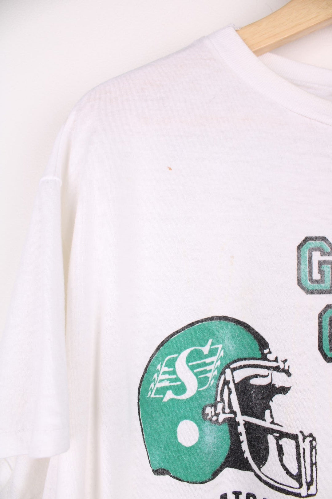 Vintage 1989 CFL Grey Cup Saskatchewan Roughriders vs Hamilton Tiger Cats tee in white with helmet face-off graphic on the front and photo of trophy on the back.